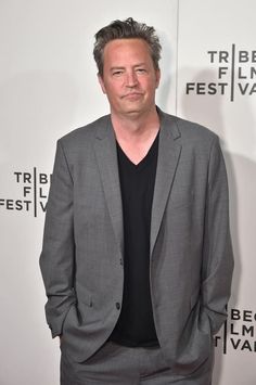 a man in a suit and black shirt standing on the red carpet at an event