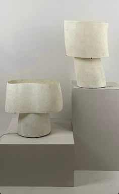 two white lamps sitting on top of pedestals in front of a gray wall and floor