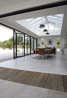 a large open room with wooden floors and glass doors on the ceiling, leading to an outdoor dining area