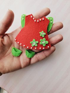 a hand holding a small red piece of felt with green leaves and flowers on it