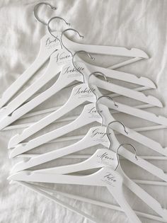 a bunch of white hangers with names on them sitting on a tablecloth covered bed