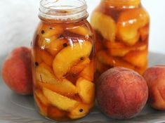 two jars filled with sliced peaches on top of a white plate next to apples