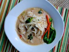 a white bowl filled with noodles and veggies on top of a striped place mat