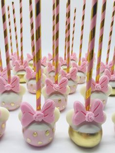 there are many pink and white cupcakes with bows on them that have candles sticking out of them