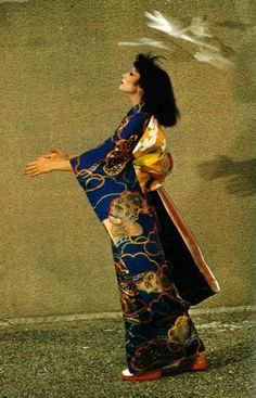 a woman in a blue and gold kimono throwing a white bird