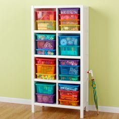 a white shelf filled with lots of plastic containers and toys in front of a green wall