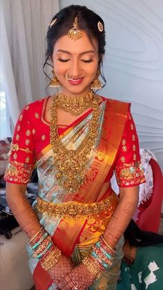 a woman in a red and gold sari is holding her hands together as she smiles