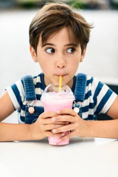 a young boy drinking a drink with a straw in his mouth and looking up at the camera