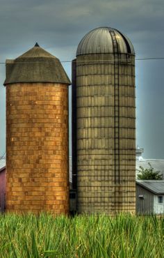 two large silos sitting next to each other on top of a lush green field