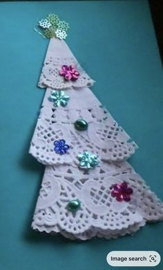 a small white christmas tree made out of doily on a blue surface with green and pink flowers