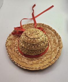 a straw hat with a red ribbon tied around the brimmed crown on a white surface