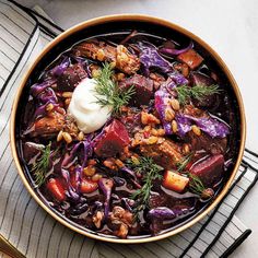 a bowl filled with meat and vegetables on top of a striped cloth next to a spoon