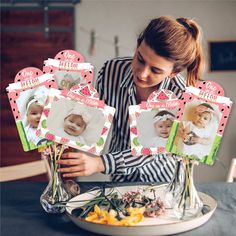 a woman holding up some baby pictures on top of a plate with flowers in front of her