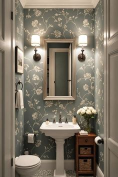 a white toilet sitting under a bathroom mirror next to a sink in a room with blue wallpaper