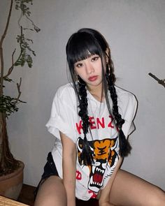 a young woman sitting on top of a wooden table next to a potted plant