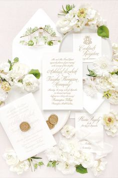 the wedding stationery is laid out on top of each other, with white flowers and greenery