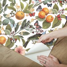 a person cutting paper on top of a table with oranges and other fruit in the background