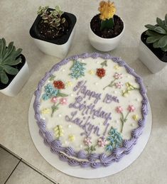 a birthday cake sitting on top of a table next to succulents and potted plants