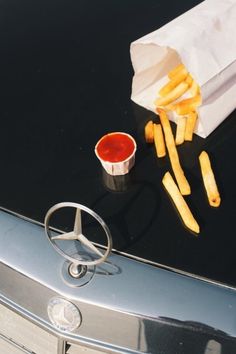 french fries and ketchup are sitting on the hood of a mercedes benz car