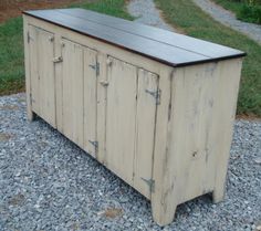 a wooden cabinet sitting on top of a gravel ground next to a grass covered field