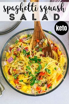 a glass bowl filled with spaghetti salad next to a wooden spoon and utensils