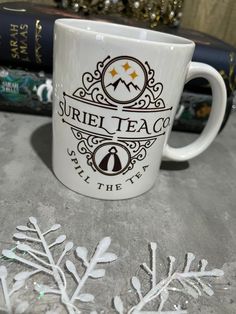 a white coffee mug sitting on top of a table next to snowflakes and books