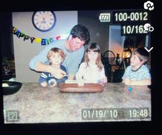 a man and two children sitting at a table with a clock on the wall behind them