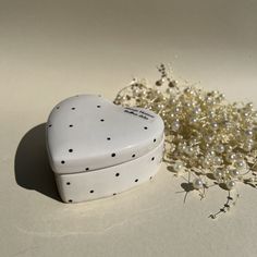 a white heart shaped box sitting next to some flowers and pearls on a table top