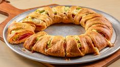 a croissant filled with meat and cheese on top of a metal plate next to a wooden cutting board