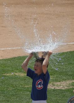 a young boy holding up a baseball trophy in front of his head with water pouring out of it