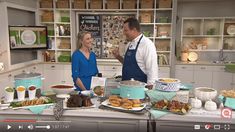 a man and woman standing in front of a table full of food on the tv screen