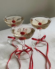 three martini glasses with cherries in them on a white table cloth covered tablecloth