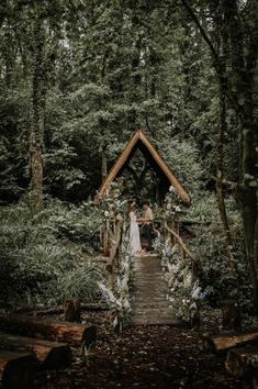 a bride and groom standing on a wooden bridge in the woods surrounded by greenery