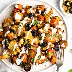 a white plate topped with stuffing next to a bowl of vegetables and a silver fork