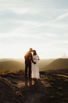 a man and woman standing on top of a dirt hill next to each other with the sun behind them