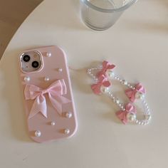 a pink phone case with pearls and bows on it next to a glass of water