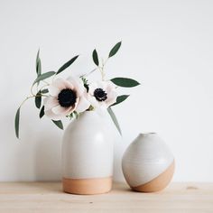 two white vases with flowers in them sitting on a wooden table next to each other