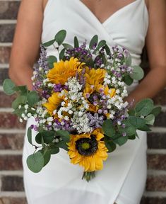 a bride holding a bouquet of sunflowers and baby's breath in front of a brick wall