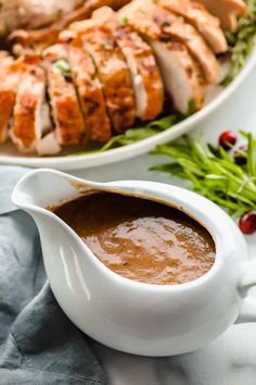 a white gravy pitcher filled with sauce next to a platter of meat