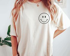 "Smiley Face Comfort Colors Shirt, Happy T-shirt, Smiley Minimal Shirt, Retro Smiley Face Shirt, Smiley Tee, Happy Face Shirt, Gift for Her HOW TO ORDER Please, check and review all photos Choose your size from the drop-down menu and add each shirt to your cart one at a time. Click add to cart. You can go back to add more product Click \"Proceed to check out\" When you check out, you can add a note to the seller for any request Youth, toddler unisex adults round neck shirts are available in all colors listed on the drop-down menu. Designs are printed one color in the front and back of the t-shirt. ALL OF OUR T-SHIRTS ARE FROM U.S.A CARE INSTRUCTIONS Wash inside out, gentle cycle, cold water, tumble dry low, medium iron PRODUCTION AND SHIPPING Processing is 1-3 days. First Class Shipping is Everyday Funny Print Crew Neck Shirt, Everyday Crew Neck Shirt With Funny Print, Everyday Relaxed Fit Top With Smiley Face, Trendy Smiley Face Tops For Everyday, Relaxed Fit Smiley Face Top For Everyday, Everyday Relaxed Fit Smiley Face Top, Casual Smiley Face Top, Cute White T-shirt With Smiley Face, Funny White T-shirt With Smiley Face