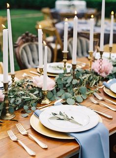 the table is set with candles, plates and greenery for an elegant wedding reception