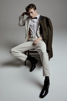 a man sitting on top of a wooden bench wearing a suit and bow tie with his hands in his ears