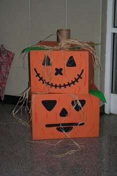 two cardboard boxes decorated like pumpkins with faces painted on them, sitting in front of a door