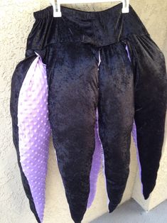 two black and purple pants hanging up on a white wall with polka dot trims