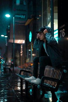 a man sitting on a bench in the rain talking on his cell phone at night