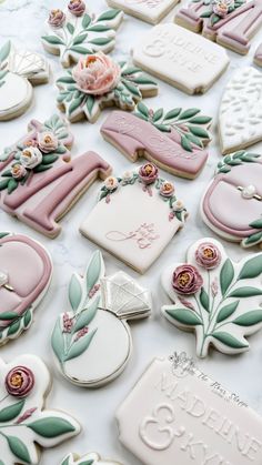 many decorated cookies on a table with flowers and leaves in the middle one cookie has been cut out to look like letters