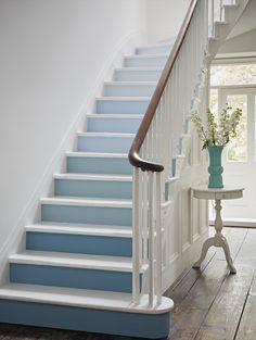 a blue and white stair case next to a table with a vase on top of it