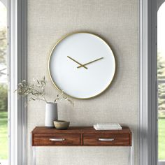 a white clock mounted to the side of a wall next to a vase with a plant