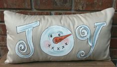 a snowman pillow sitting on top of a wooden bench next to a brick wall