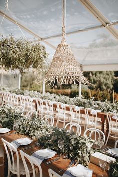 tables and chairs are set up for an outdoor wedding with greenery hanging from the ceiling